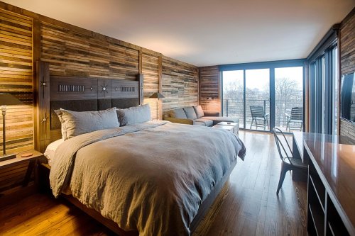 Cozy hotel room with wooden walls, a large bed, seating area, and balcony access overlooking a scenic view.