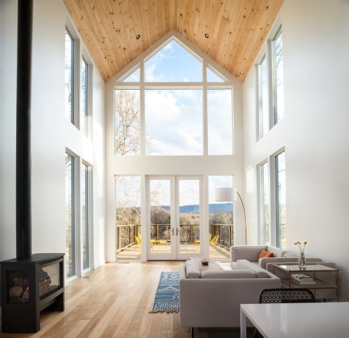 Bright, modern living room with large windows, wooden ceiling, and a cozy seating area overlooking a scenic view.