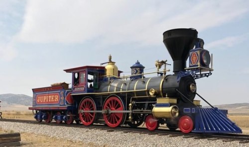 A vintage steam locomotive named "Jupiter" with colorful details, parked on a railway track against a cloudy sky.