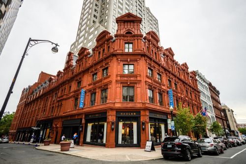 Historic red brick building with ornate architecture, featuring shops and a tall modern building in the background.