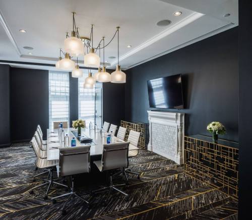 Modern conference room with a long table, stylish chairs, a chandelier, and a TV on a dark wall.