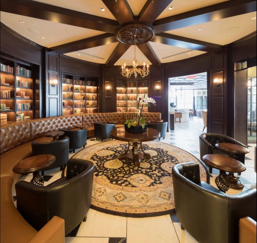 Elegant lounge with a circular seating area, bookshelves, a chandelier, and a decorative rug. Warm, inviting atmosphere.