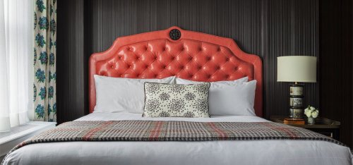 A stylish bedroom featuring a tufted coral headboard, white bedding, and a decorative pillow on a cozy plaid throw.
