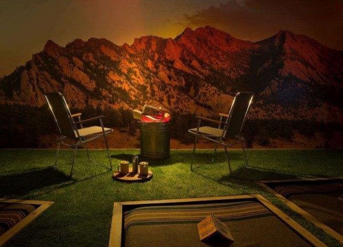 Two chairs facing a fire pit on a grassy area, with a backdrop of mountains at sunset. Cozy outdoor setting.