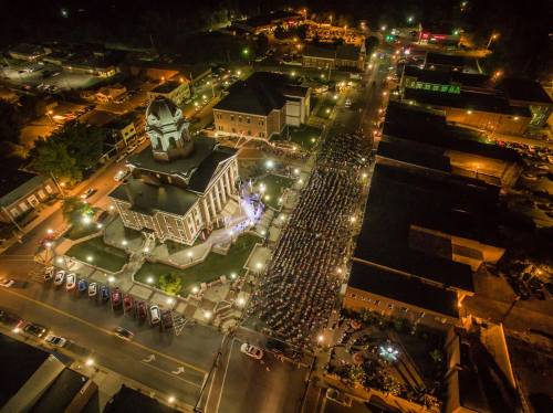 Aerial view of a large crowd gathered at night around a historic courthouse, with city lights illuminating the scene.