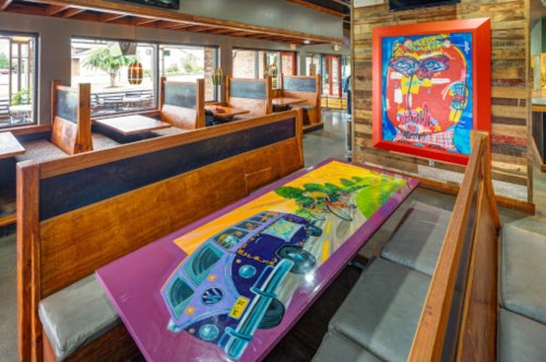 Colorful restaurant interior featuring vibrant wall art and a unique table design with a vintage car illustration.