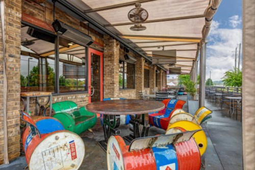 Outdoor seating area with colorful barrel chairs and a round table, surrounded by brick walls and a canopy.