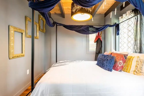 Cozy bedroom with a four-poster bed, draped fabric, decorative pillows, and framed art on the walls.