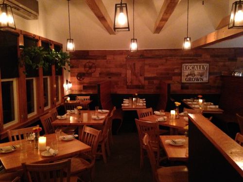 Cozy restaurant interior with wooden tables, warm lighting, and rustic decor, featuring plants and a "Locally Grown" sign.