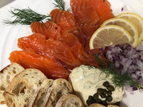 Sliced smoked salmon with lemon, red onion, dill, capers, and toasted bread on a white plate.
