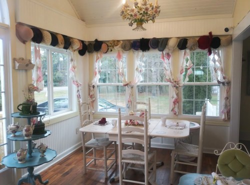 A cozy dining area with a table, chairs, and a decorative display of hats along the windows.