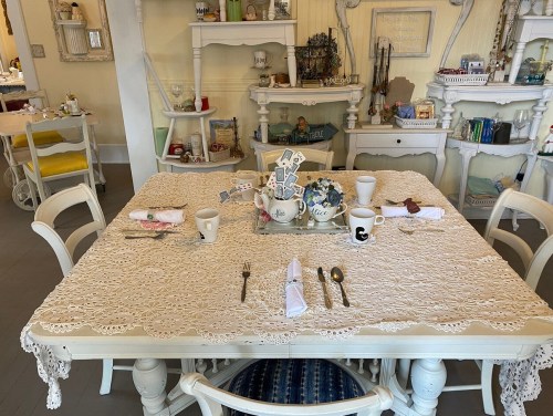 A beautifully set dining table with a lace tablecloth, floral centerpiece, and elegant dishware in a cozy room.