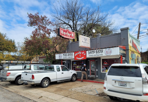 A small restaurant with a sign reading "Shrimp Buster" and "Harbkr," surrounded by parked white trucks.