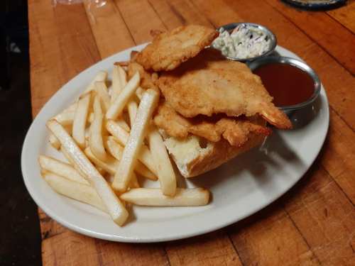 A plate with fried fish fillets, French fries, coleslaw, and dipping sauce on a wooden table.