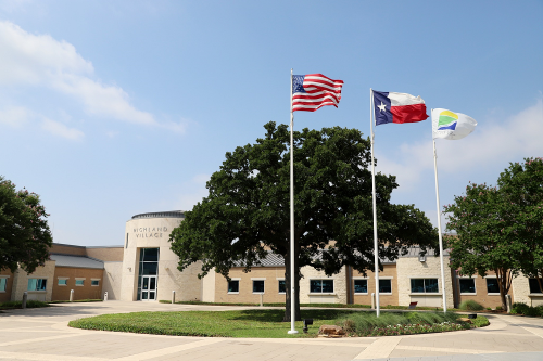 Exterior of Highland Village City Hall with American, Texas, and city flags flying in front of a modern building.