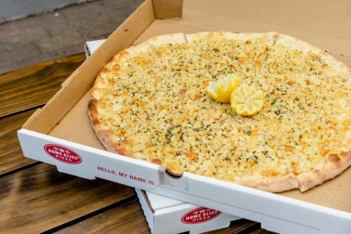 A large pizza topped with herbs and lemon slices, placed in an open pizza box on a wooden table.