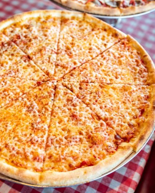A large cheese pizza sliced into eight pieces, resting on a checkered tablecloth.