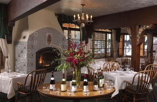 Cozy restaurant interior with a fireplace, elegant table settings, and a floral centerpiece surrounded by wine bottles.