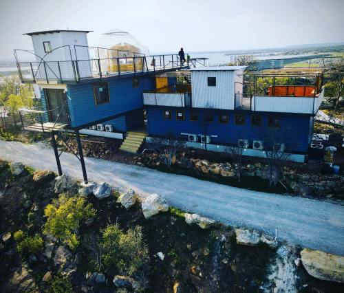 A modern, multi-level house with a rooftop deck, surrounded by rocky terrain and a pathway leading up to it.