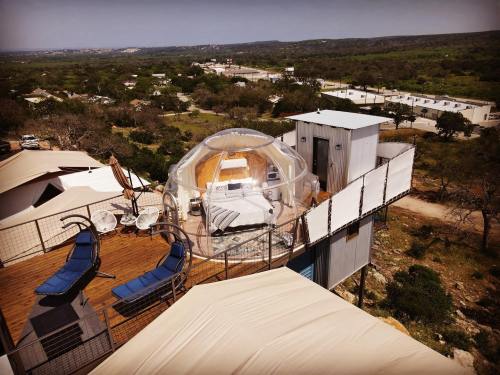 A transparent dome on a wooden deck, surrounded by chairs, overlooking a scenic landscape and nearby buildings.