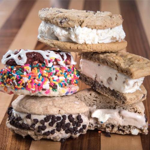 A stack of four ice cream sandwiches made with various cookies and colorful sprinkles, resting on a wooden surface.