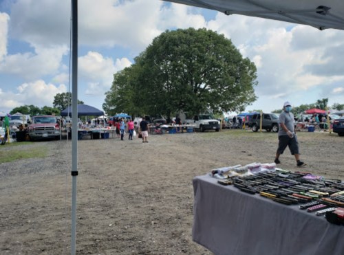 A bustling outdoor market scene with various stalls, vehicles, and people walking under a cloudy sky.