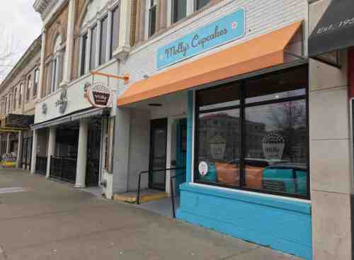 Exterior of Molly's Cupcakes shop with a blue and orange awning, featuring large windows and a sidewalk view.