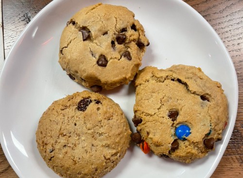 Three large cookies on a white plate: two with chocolate chips and one with a blue candy.