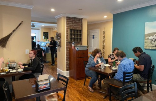 A cozy restaurant scene with diners enjoying meals at tables, and staff working in the background.