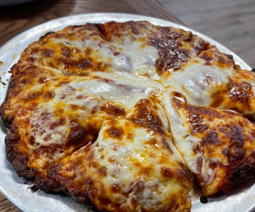A freshly baked pizza with melted cheese and a golden-brown crust, sliced into wedges on a silver platter.