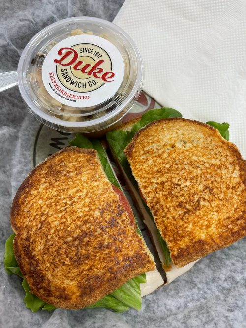 A toasted sandwich with lettuce and tomato, alongside a cup of Duke's sandwich co. dessert.