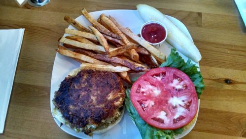 A plate with a crispy burger patty, fresh tomato slices, lettuce, fries, a pickle, and a small cup of ketchup.