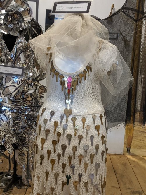 A white dress adorned with various keys, featuring a lace design and a sheer veil.