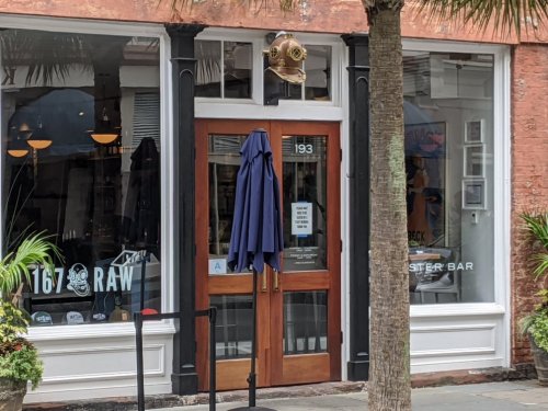 A storefront with wooden doors, a diving helmet decoration, and an umbrella outside, surrounded by palm trees.