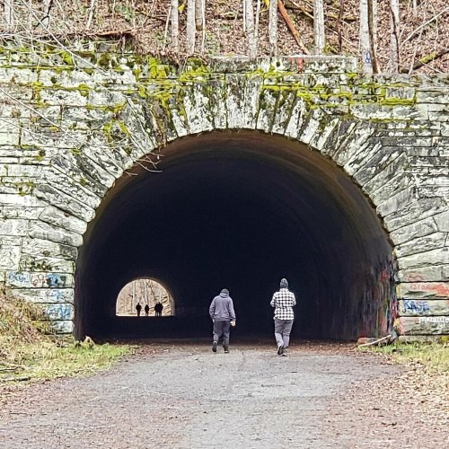 Two figures walk towards a tunnel entrance, with another group visible in the distance inside the tunnel.