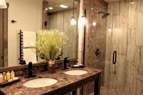A modern bathroom featuring double sinks, a glass shower, and decorative plants on a granite countertop.