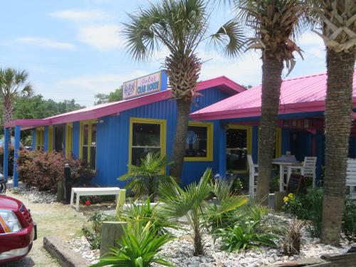 A colorful blue restaurant with a pink roof, surrounded by palm trees and tropical plants on a sunny day.