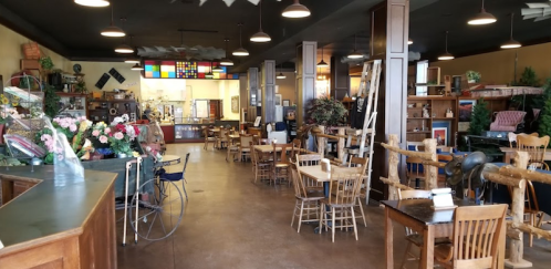 A spacious vintage shop with wooden furniture, decor items, and a cozy atmosphere, featuring plants and displays.