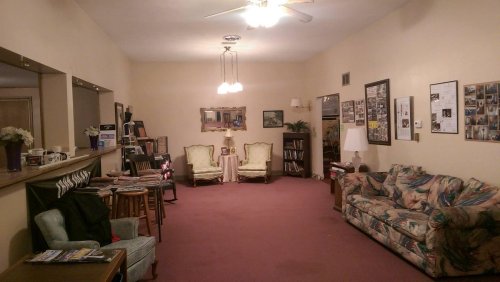 A spacious living room with a carpet, two armchairs, a couch, and various decorations on the walls and shelves.
