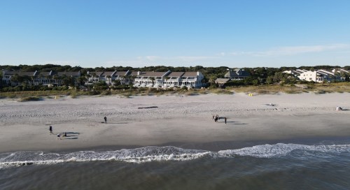 A serene beach scene with people walking along the shore and beach houses in the background under a clear blue sky.