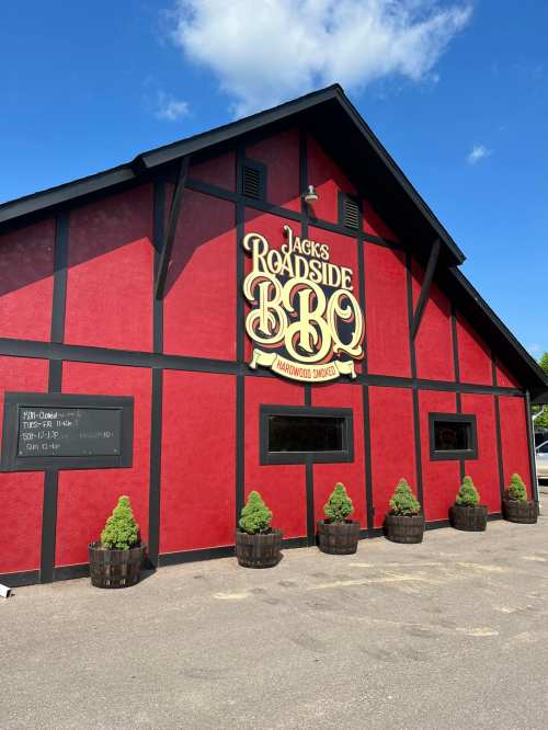 A red barn-style building with a sign reading "Jack's Roadside BBQ" and decorative plants in front.