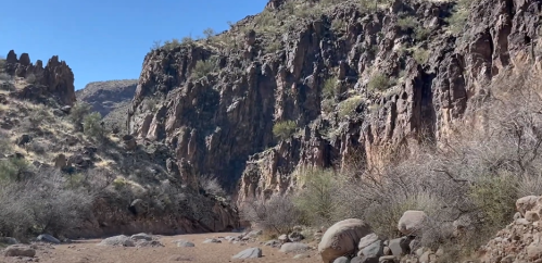 A rocky canyon landscape with steep cliffs and sparse vegetation under a clear blue sky.