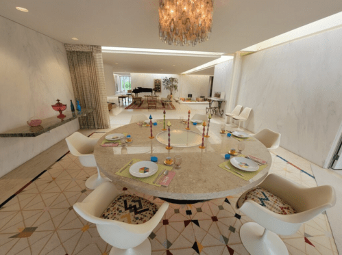 A modern dining room featuring a round marble table, colorful candles, and stylish white chairs, with elegant decor.