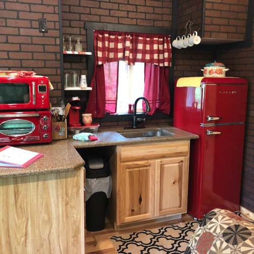 Cozy kitchen with red appliances, wooden cabinets, and a checkered curtain by the window.