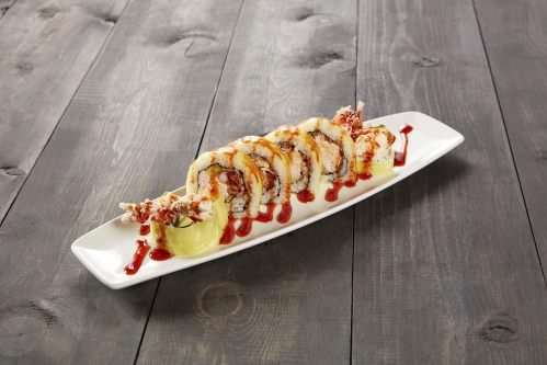 A plate of sushi rolls topped with crispy shrimp and drizzled with sauce, served on a wooden table.