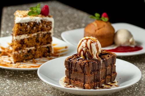 A plate with three desserts: a layered cake, a muffin, and a brownie topped with ice cream and caramel sauce.