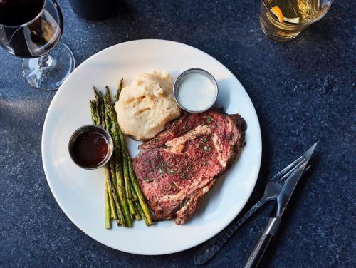 A plate with a juicy steak, mashed potatoes, asparagus, and sauces, accompanied by a glass of red wine.