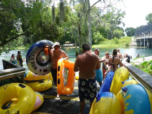 People at a riverbank preparing inflatable tubes for a day of floating and fun in the water. Lush greenery surrounds them.