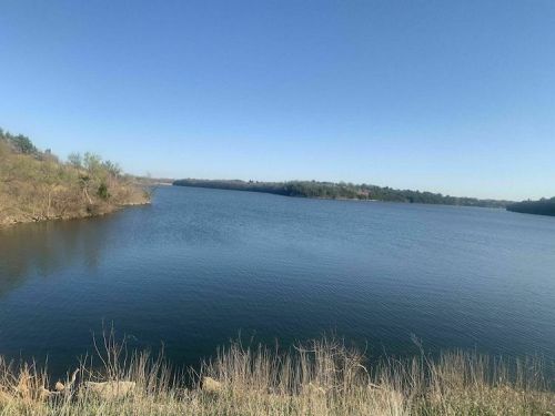 A serene lake surrounded by trees under a clear blue sky, with calm water reflecting the landscape.