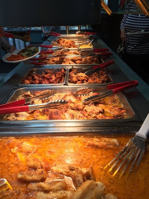 A buffet display featuring various dishes, including meats and sides, with tongs for serving.